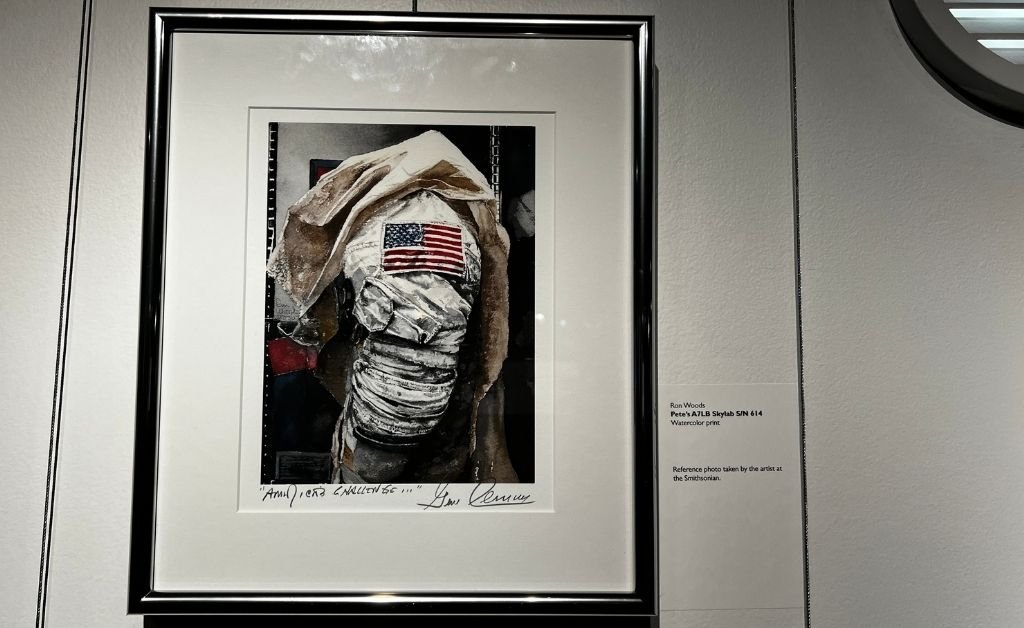 Framed watercolor print titled Pete’s A7LB Skylab S/N 614 by Ron Woods, showing a close-up of a Skylab spacesuit with an American flag. 