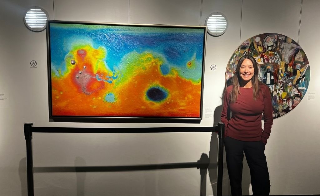 Karen LeBlanc standing beside E. Lee Wilson Jr.’s Robots of Mars, a mixed-media artwork incorporating real Martian meteorite fragments.