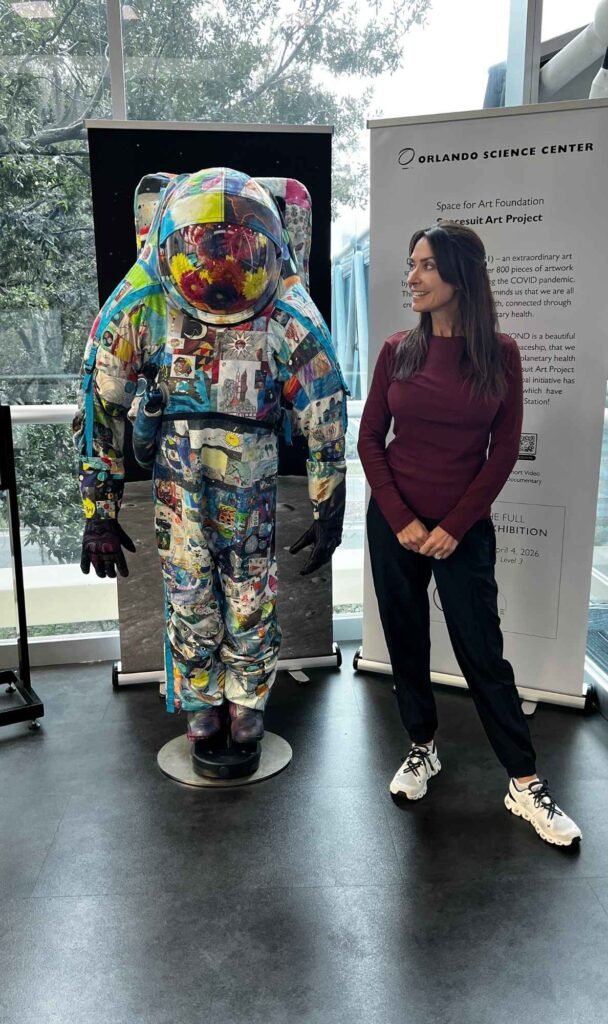 Karen standing beside the colorful patchwork Spacesuit Art Project installation at the Orlando Science Center.