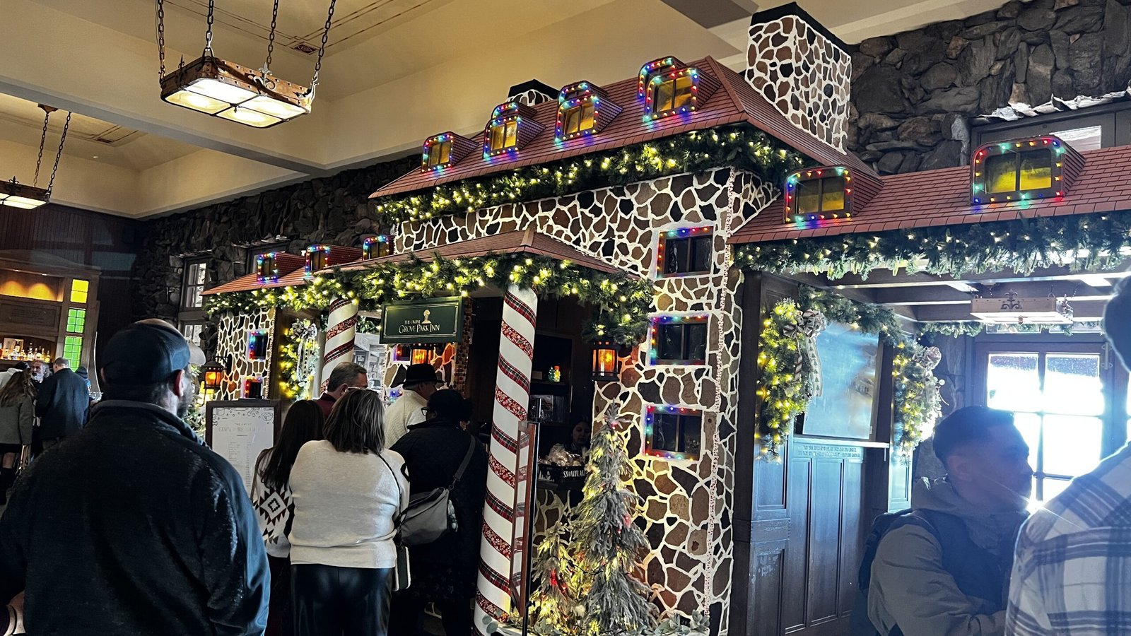 Guests viewing the Great Gingerbread House display decorated with lights and garlands inside the Omni Grove Park Inn & Spa.