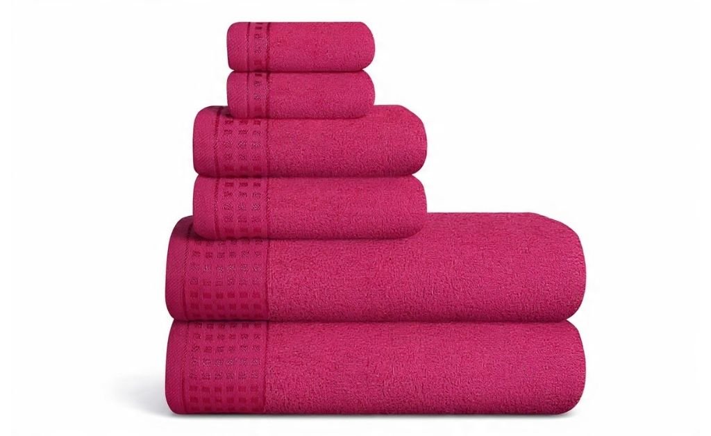 Stack of folded bath towels in deep pink arranged on a white background