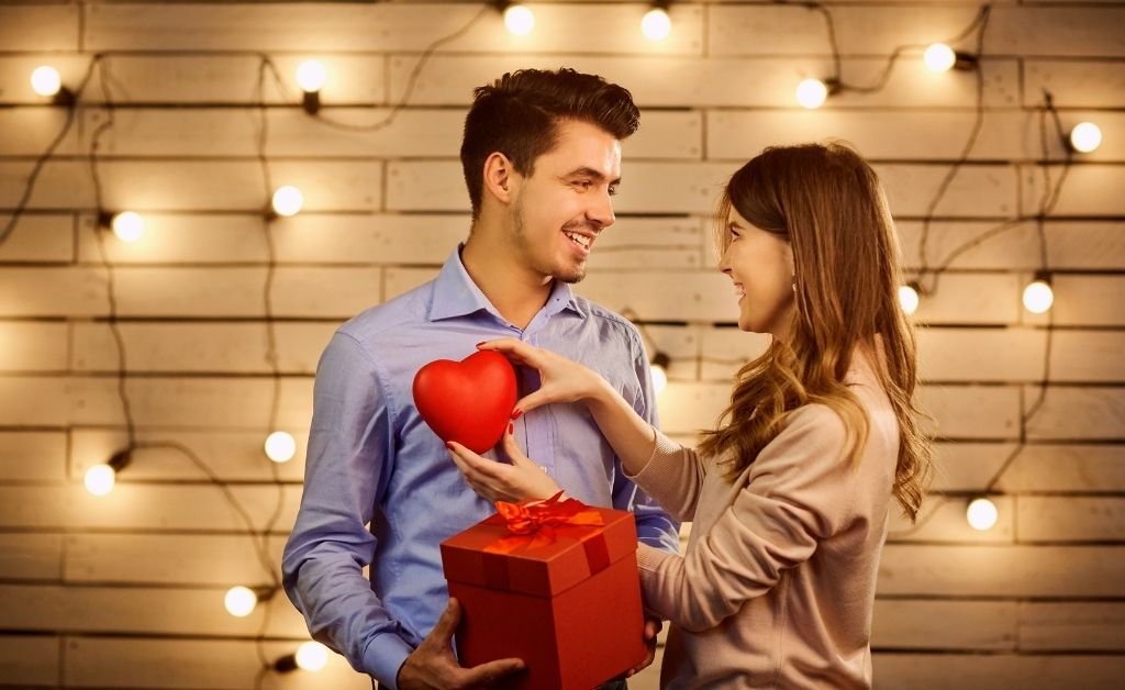 Valentine’s Day gift ideas shown as a couple exchanging a heart-shaped gift in a warm, romantic setting