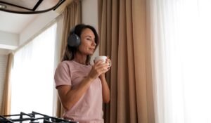 Woman wearing headphones and holding coffee cup by a window
