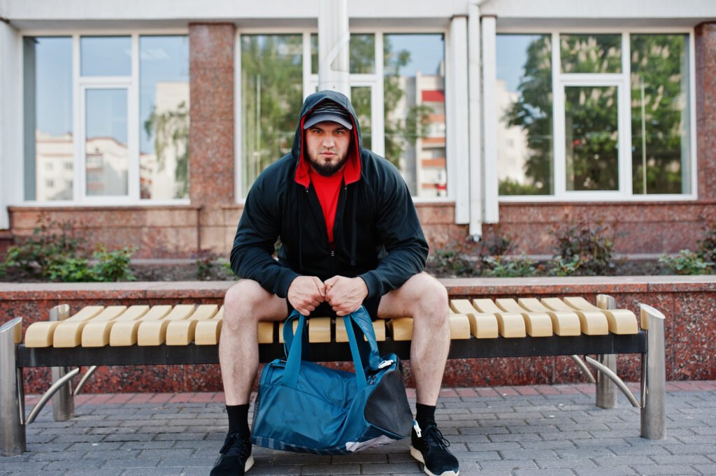 Man in hoodie sitting on bench with gym bag