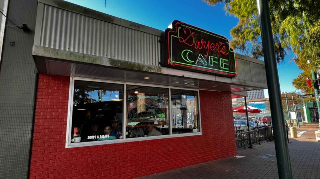 The red brick exterior facade of Dwyer's Cafe in downtown Lafayette featuring a vintage neon rooftop sign against a clear blue sky.