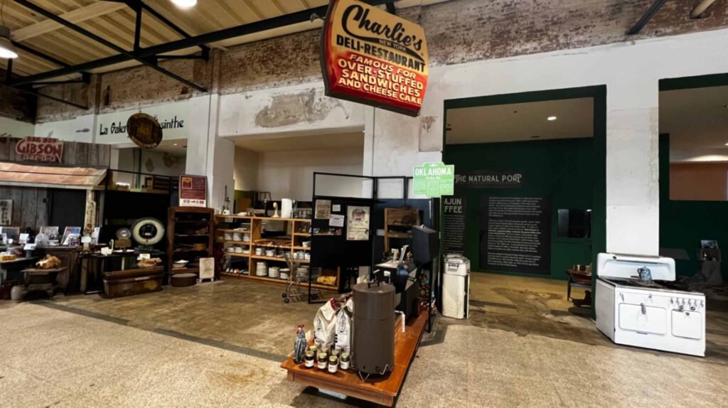 An interior exhibit room at the Southern Food and Beverage Museum featuring vintage restaurant signs like "Charlie's Deli-Restaurant," old kitchen equipment, and historical panels about New Orleans food culture.