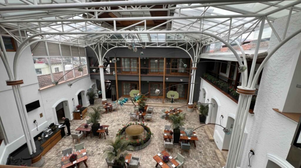 Wide high angle view of the covered interior courtyard at Hotel Mama Cuchara in Quito showing an expansive white glass roof structure over the tiled restaurant seating area below