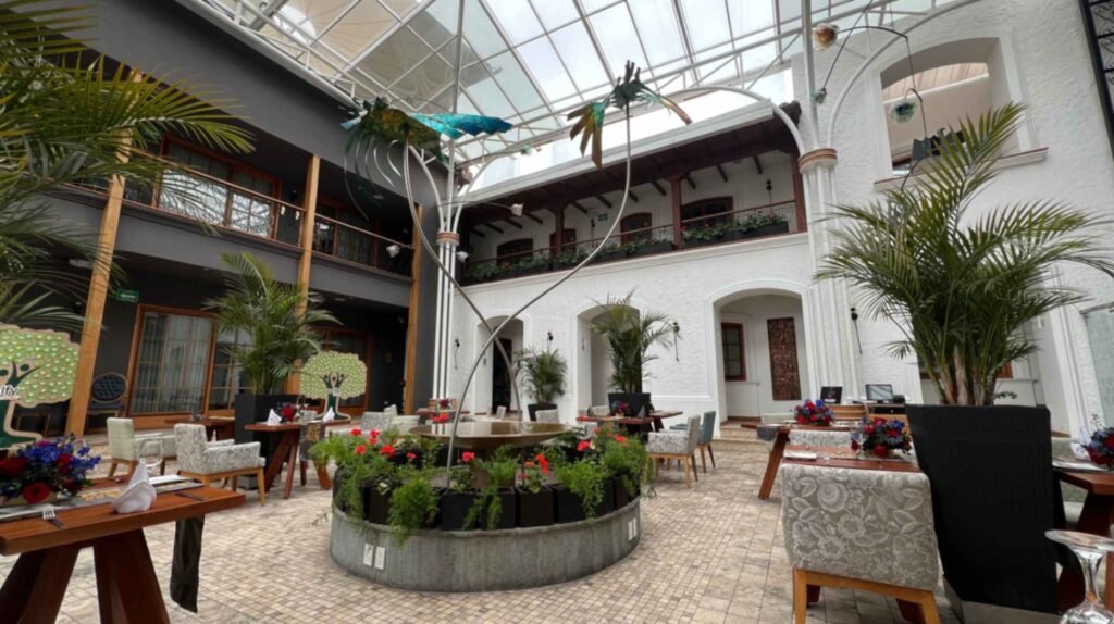 Eye level perspective of an indoor courtyard restaurant in Ecuador showing white stone arches wooden pillars potted palms and dining tables set with floral centerpieces