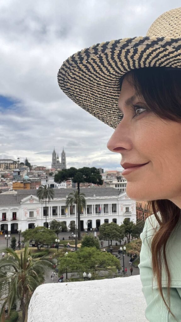 Close up profile view of a woman wearing a woven straw hat looking out over Plaza de la Independencia in Quito Ecuador with the Carondelet Palace and Basilica spires in the background